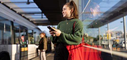 Voyageuse se tient debout à un arrête de tramway en tenant un téléphone portable à la main
