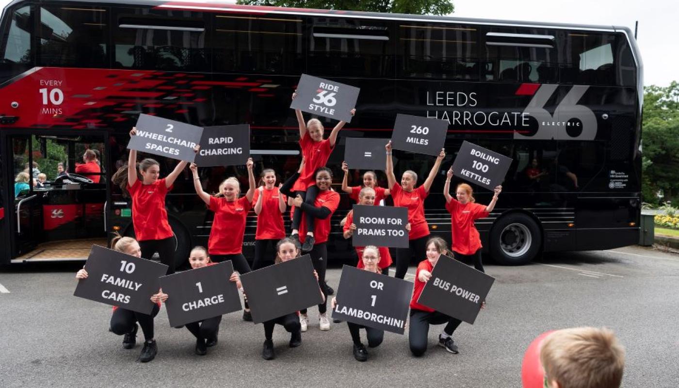 Chrildren dancing in front of Leeds Harrogate New Electric 3Buses
