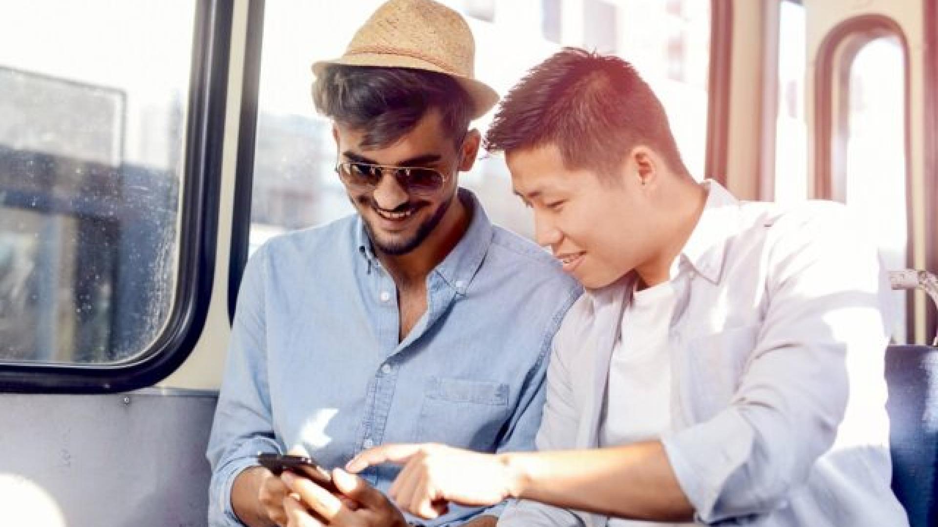 deux-jeunes-hommes-assis-dans-un-bus-regarent-un-smartphone