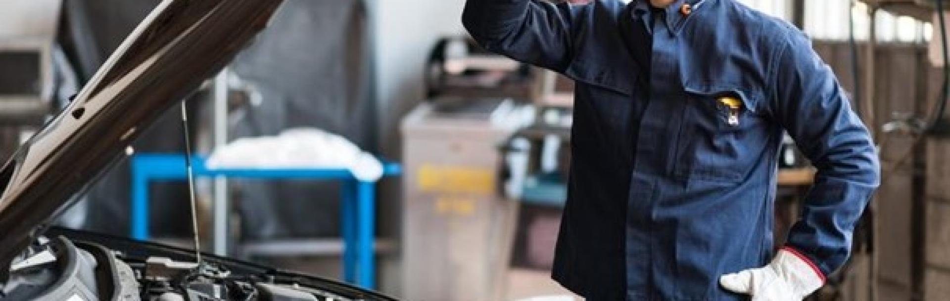 Mécanicien qui porte une casquette debout dans un garage devant un capot ouvert