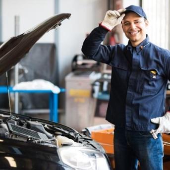 Mécanicien qui porte une casquette debout dans un garage devant un capot ouvert