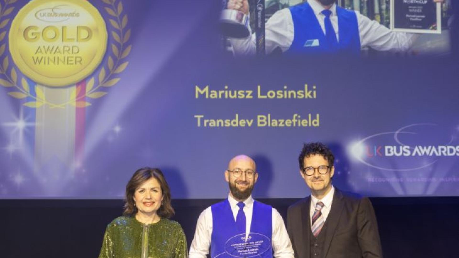 Mariusz Losinski on stage at the UK Bus Awards with his Gold trophy, BBC News host Jane Hill and Robert Jack, editor of road and rail industry journal Passenger Transport