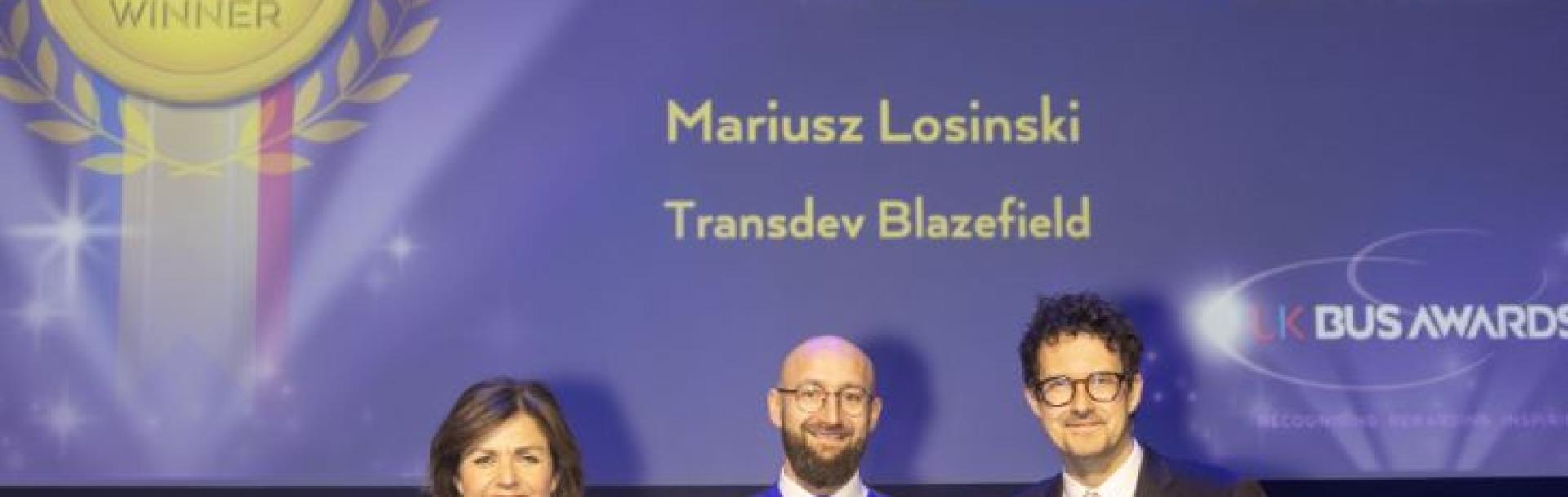 Mariusz Losinski on stage at the UK Bus Awards with his Gold trophy, BBC News host Jane Hill and Robert Jack, editor of road and rail industry journal Passenger Transport