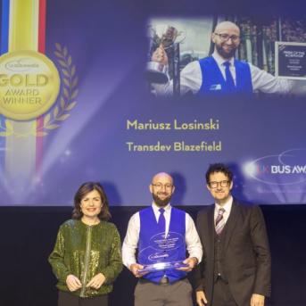 Mariusz Losinski on stage at the UK Bus Awards with his Gold trophy, BBC News host Jane Hill and Robert Jack, editor of road and rail industry journal Passenger Transport