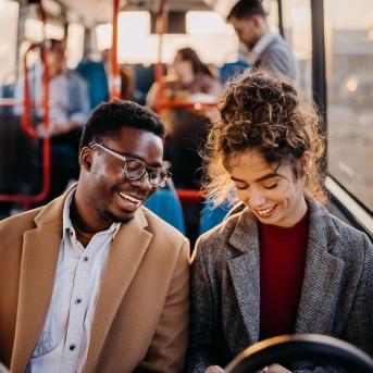 jeune homme noir avec des lunette et jeune femme blanche avec un chignon souriants assis passagers d'un bus