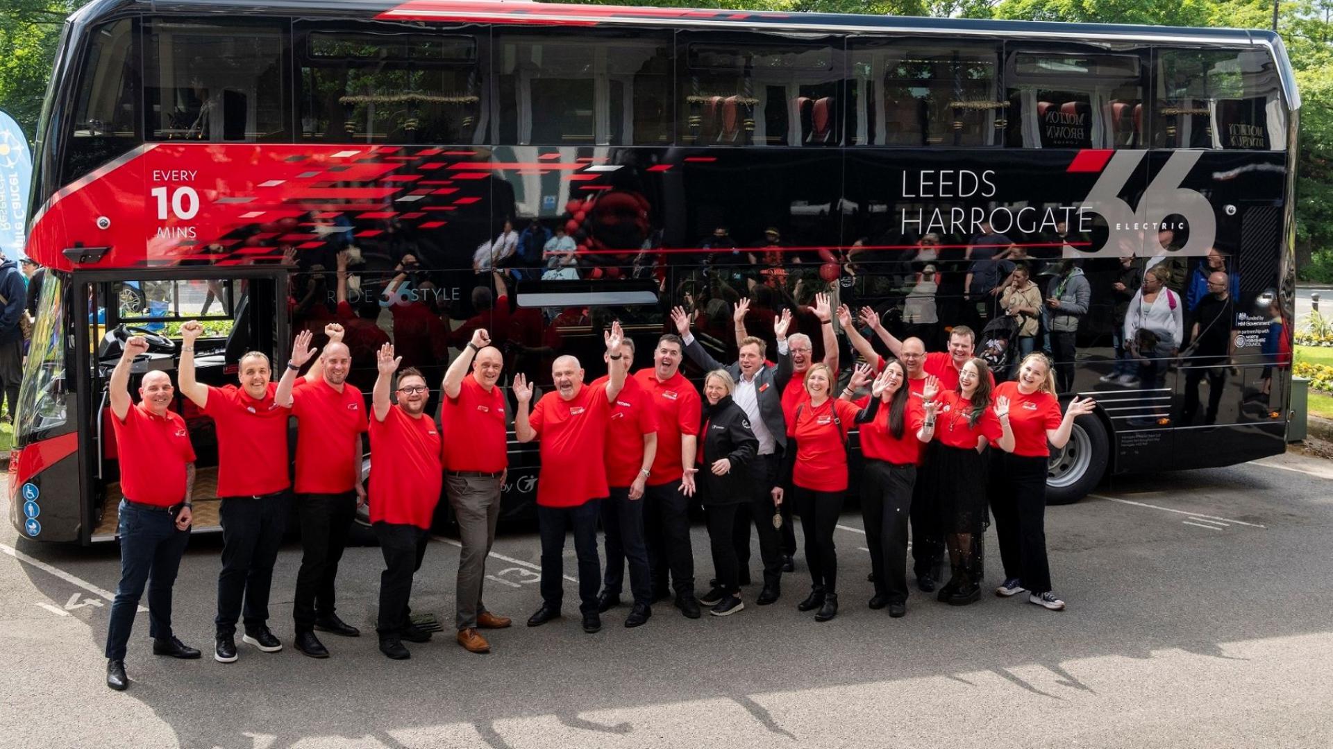 Team members of Route 26 standing in front of a bus smiling and waving
