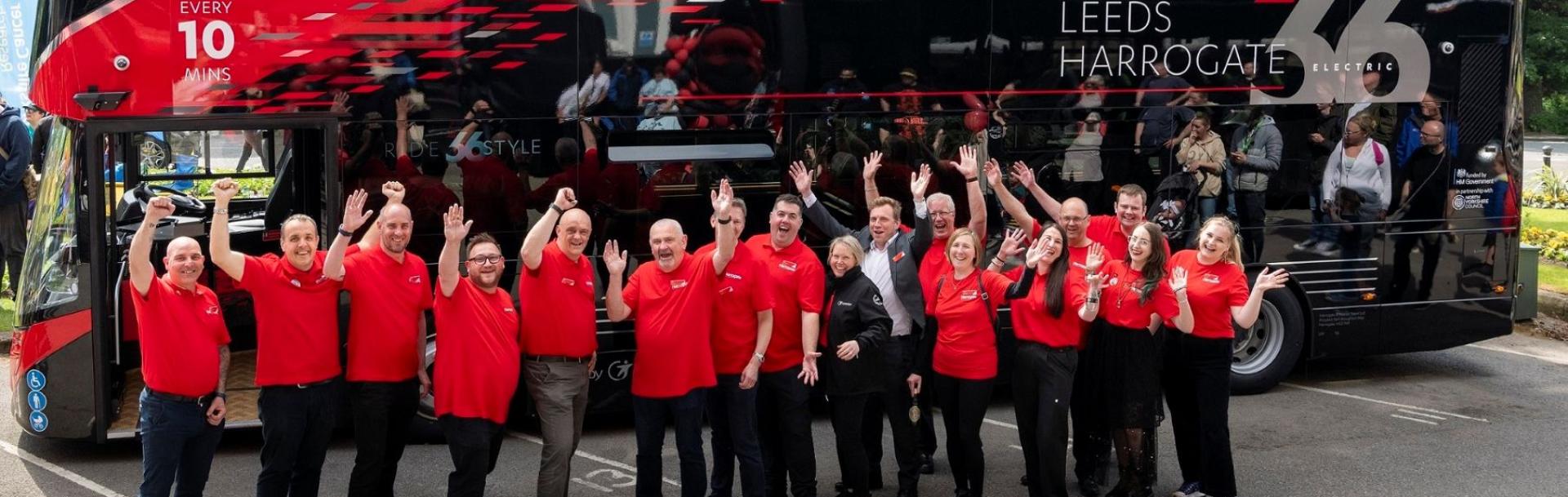 Team members of Route 26 standing in front of a bus smiling and waving