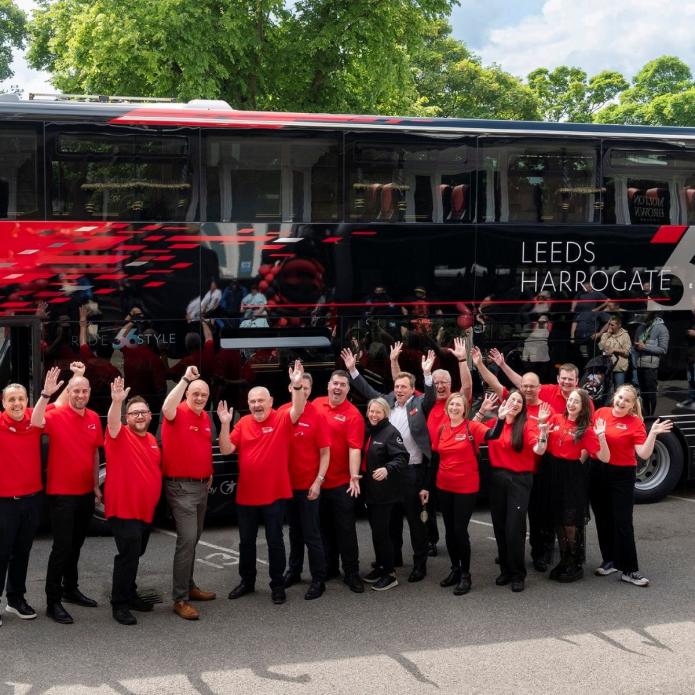 Team members of Route 26 standing in front of a bus smiling and waving