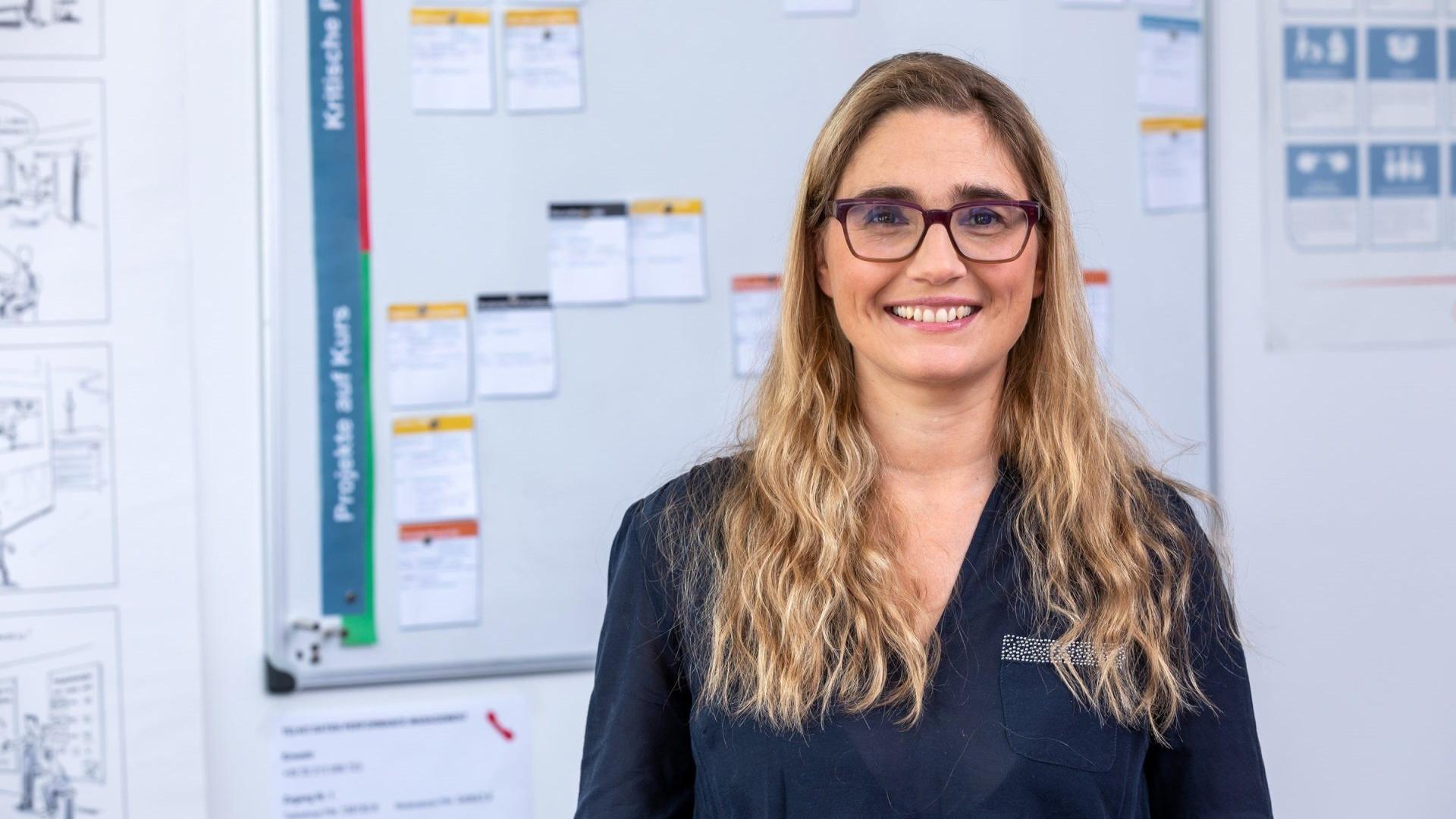 woman smiling in front of a blurred whiteboard brainstorming controller project management