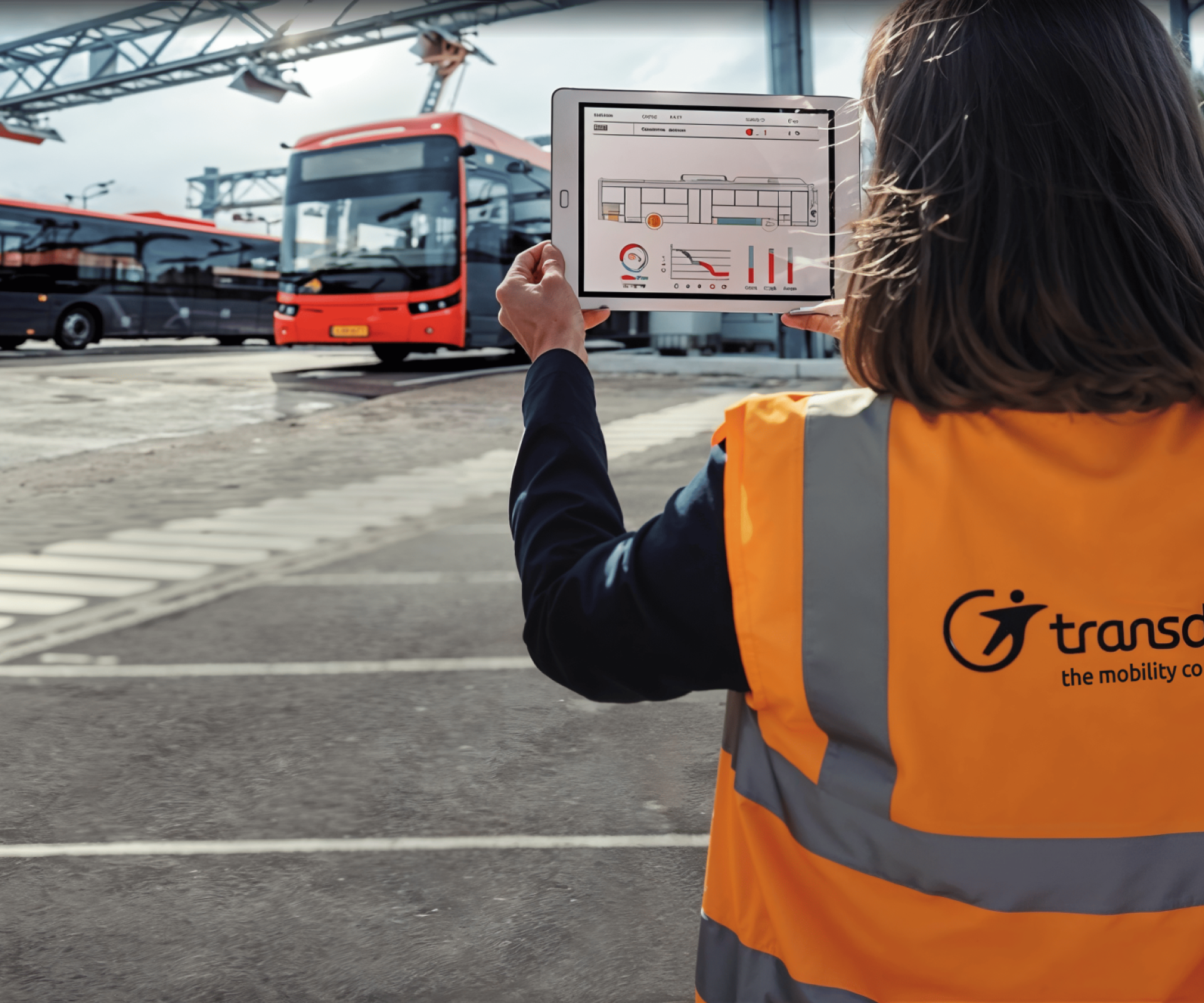 Femme au gilet orange Transdev tient en main une tablette devant des bus Transdev