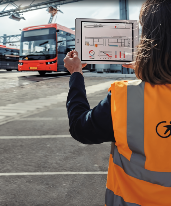 Femme au gilet orange Transdev tient en main une tablette devant des bus Transdev