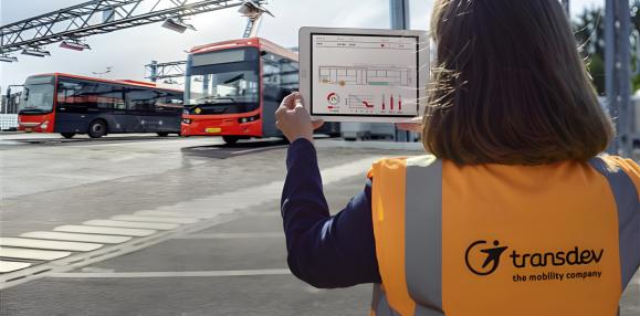 Femme au gilet orange Transdev tient en main une tablette devant des bus Transdev