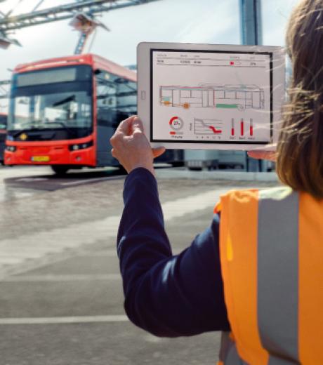 Femme au gilet orange Transdev tient en main une tablette devant des bus Transdev