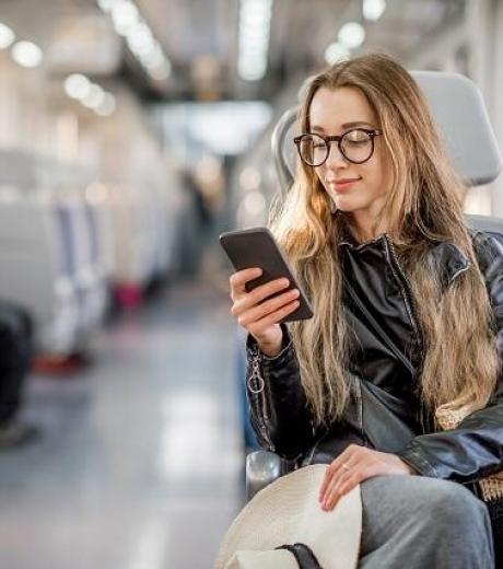 Jeune femme assise dans un train avec un smartphine à la main