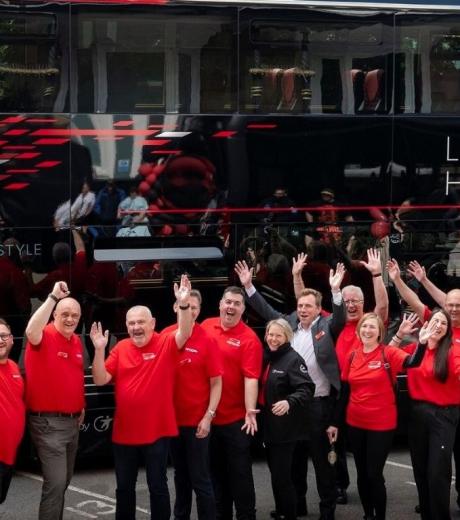 team-members-of-route-26-standing-in-front-of-a-bus-smiling-and-waving
