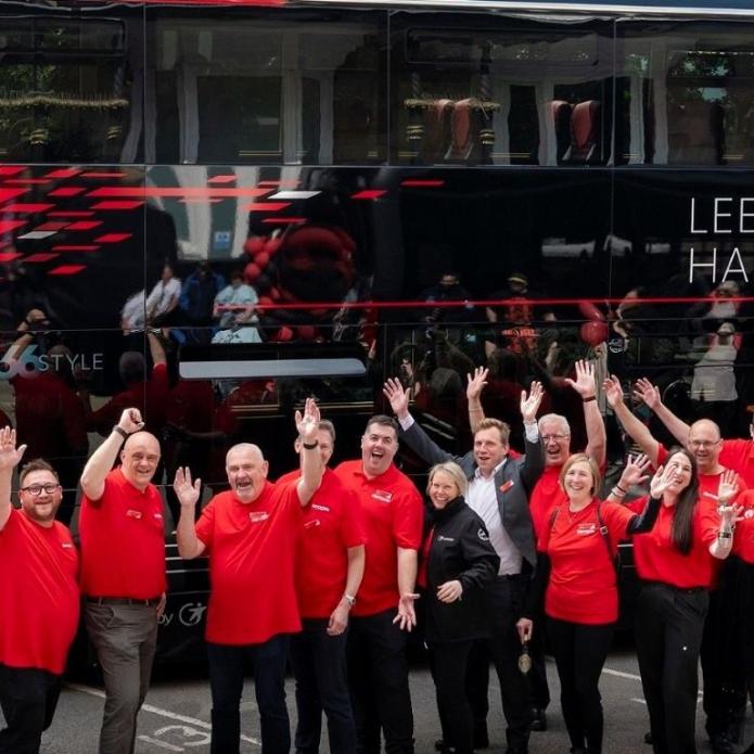 team-members-of-route-26-standing-in-front-of-a-bus-smiling-and-waving