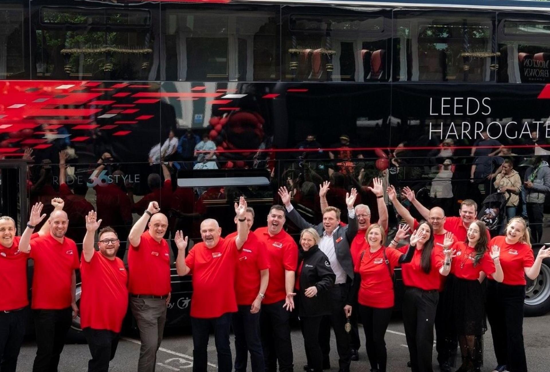 team-members-of-route-26-standing-in-front-of-a-bus-smiling-and-waving