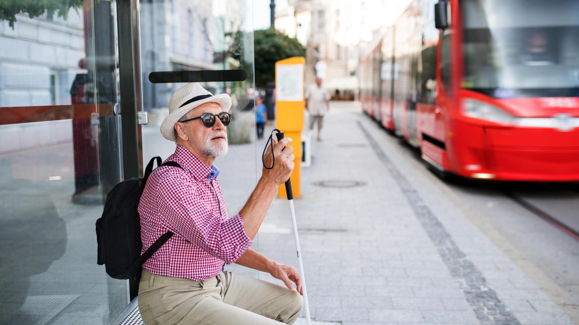 Personne malvoyante avec une cane assise à un arrêt de bus