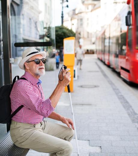 Personne malvoyante avec une cane assise à un arrêt de bus