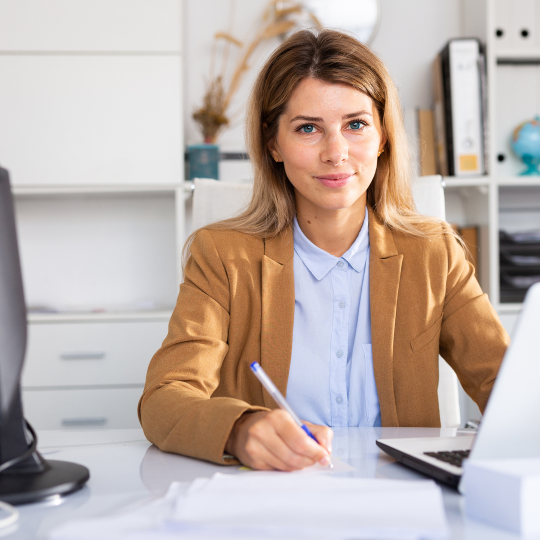 femme écrivant sur son bureau avec son ordinateur en veste marron et chemise bleu
