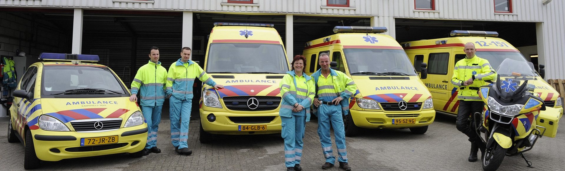 Equipe ambulanciers en uniforme jaune et bleu clair devant ambulances jaune et rouge de Kennemerland garage
