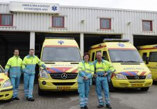 Equipe ambulanciers en uniforme jaune et bleu clair devant ambulances jaune et rouge de Kennemerland garage