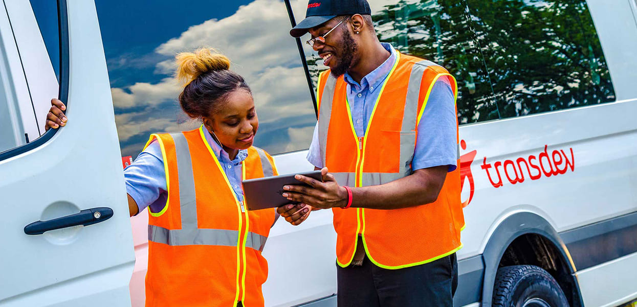 deux responsables d'exploitation parlant devant une tablette en gilet fluo orange et jaune devant un camion transdev blanc