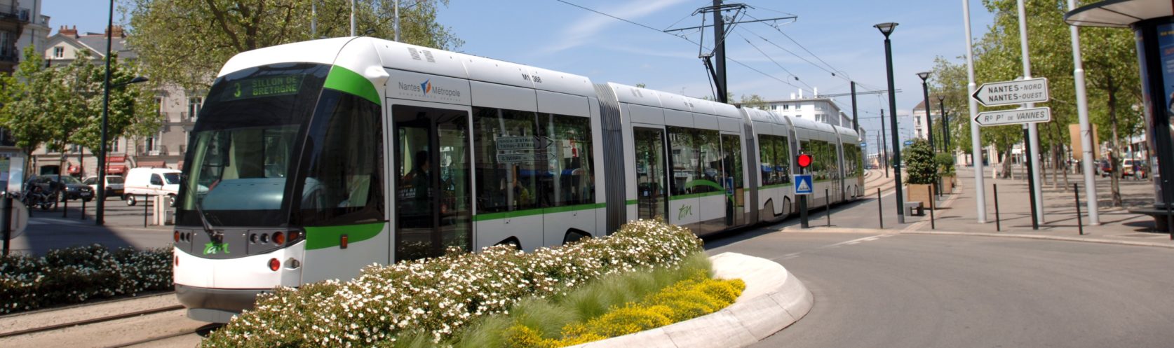 Tramway TAN vert blanc passant dans la ville de Nantes ciel bleu et drapeau français européen