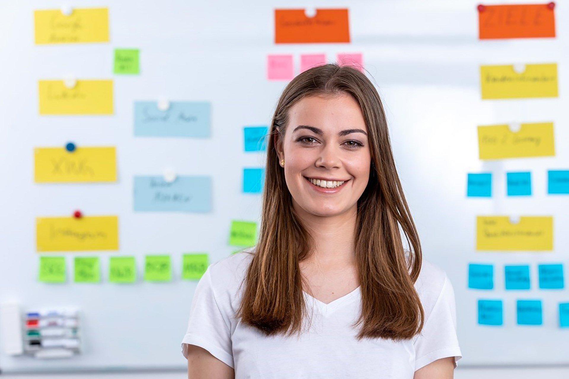 woman smiling in front of a blurred whiteboard brainstorming digital project management