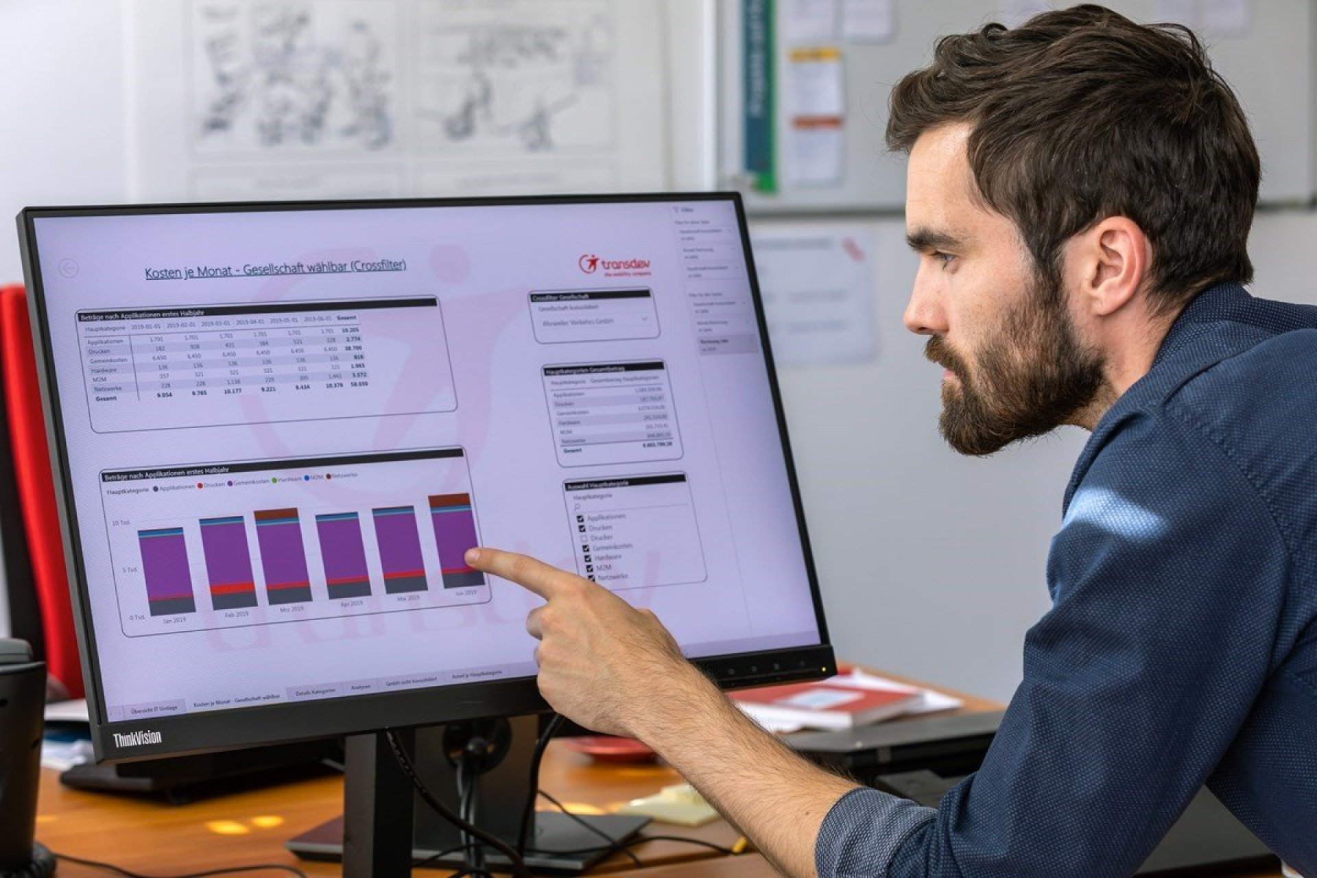 man in dark blue shirt pointing to a computer with visible statistics from transdev