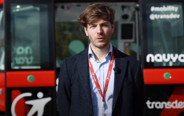 Brown man talking in front of a bus