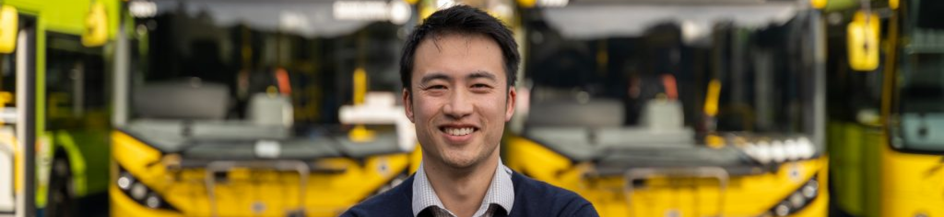 smiling man with crossed arms and blue sweater blurred background with yellow bus