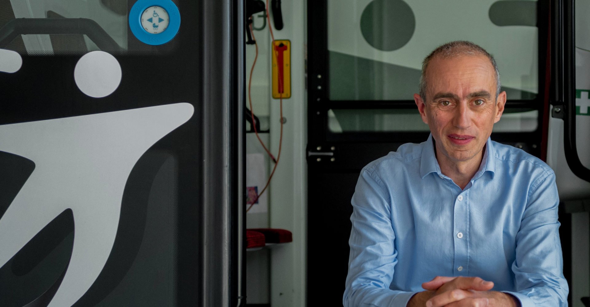 smiling older man wearing a light blue shirt sitting in a bus