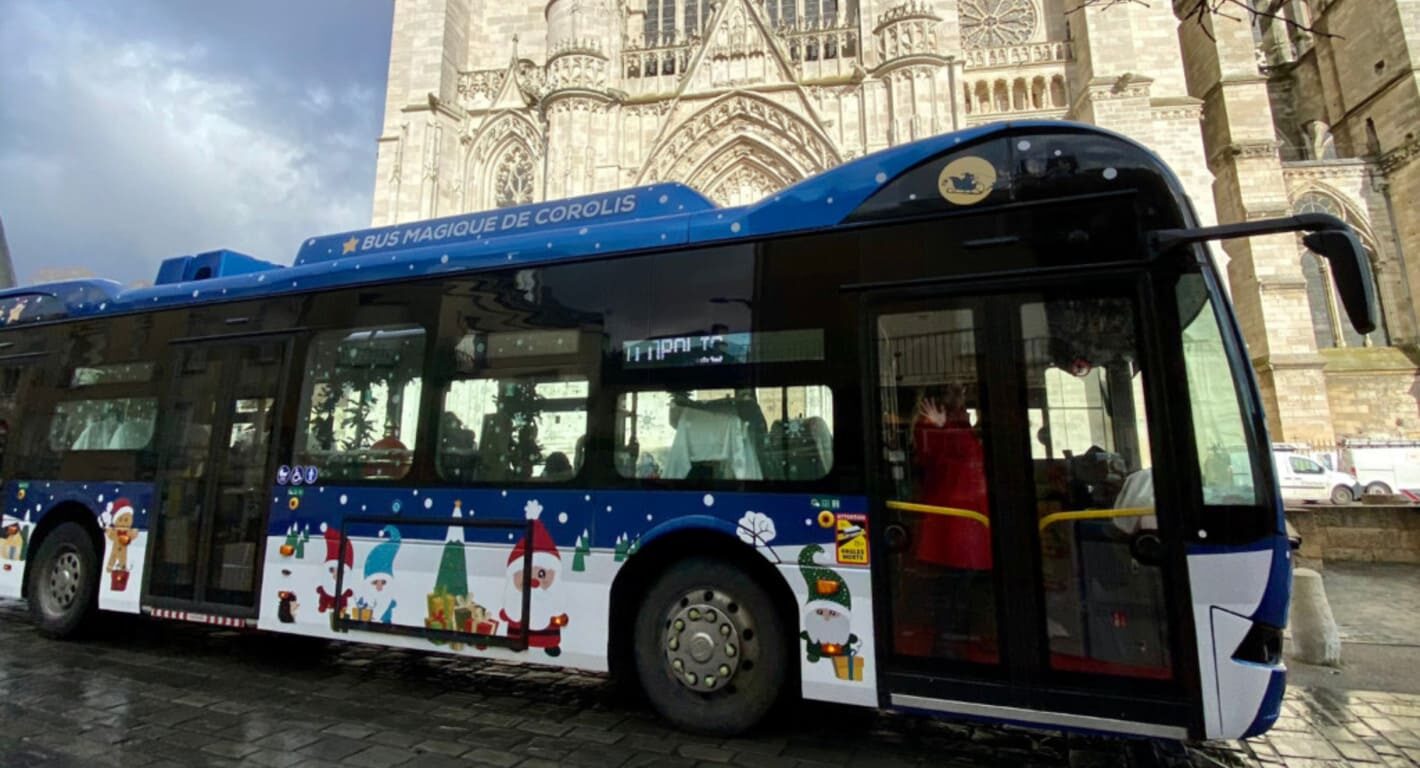 bus bleu foncé avec des stickers de noel circulant devant une cathédral