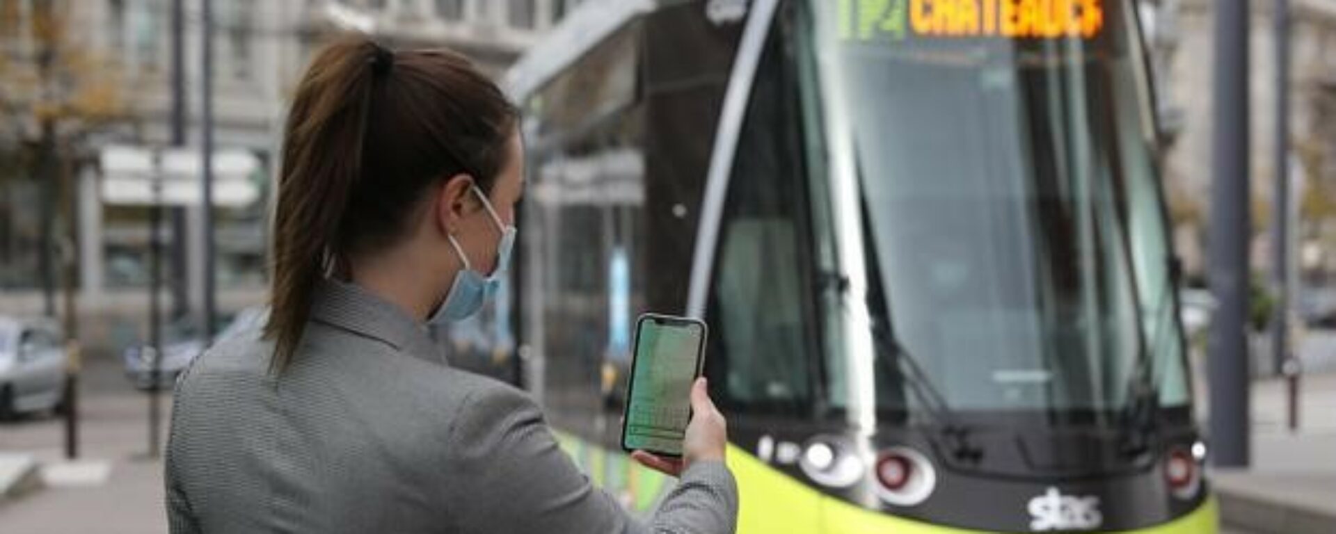 Jeune femme de dos utilise application mobile devant un tramway de Saint Etienne
