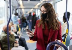 Femme masque noir manteau et pull rouge avec lunette dans bus bleu regardant son téléphone portable