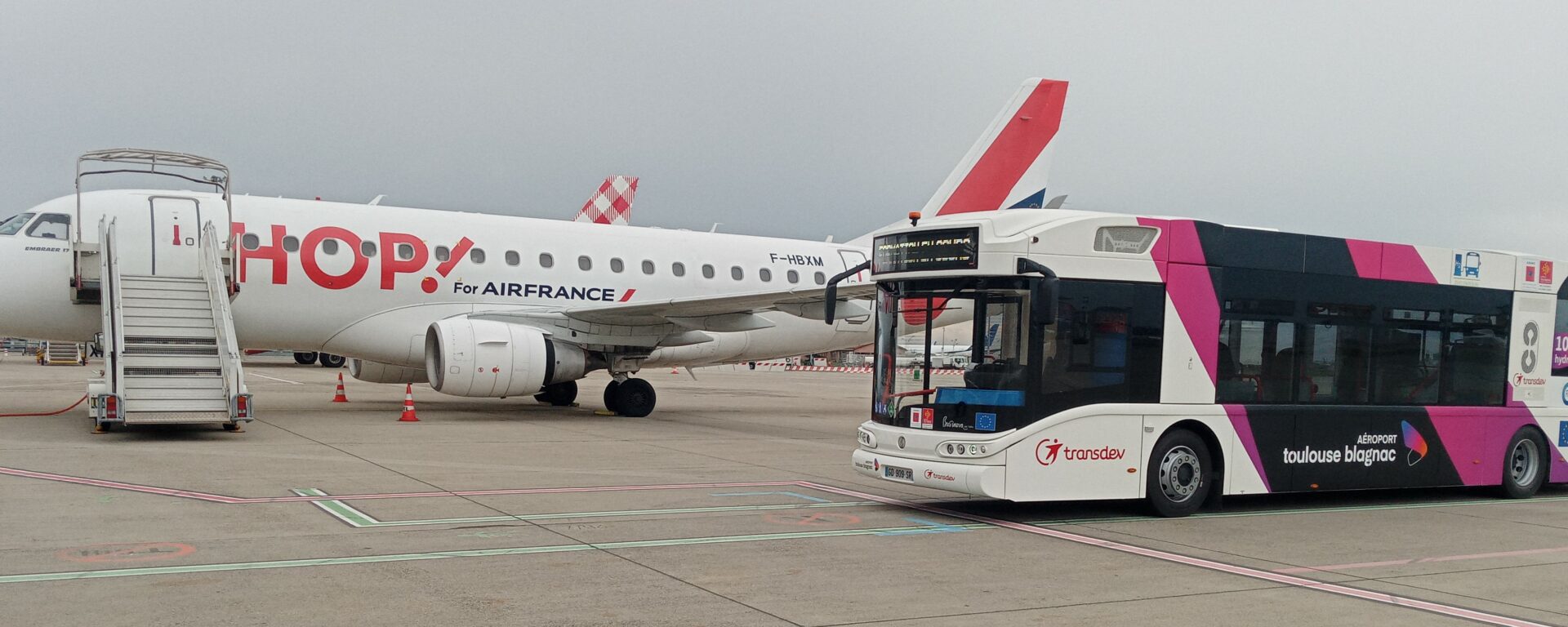 Navette Transdev Toulouse Blagnac sur le Tarmac aux côté d'un avion HOP!