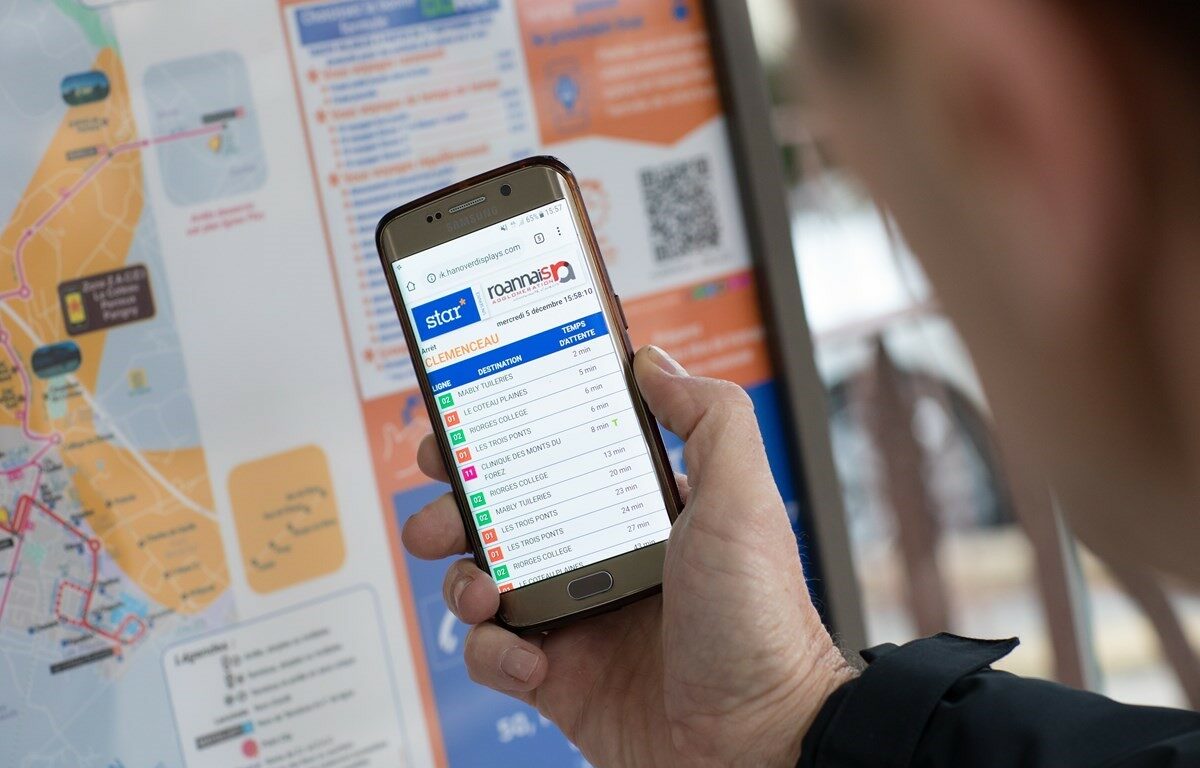Main d'homme tenant un téléphone sur l'écran duquel s'affichent des informations voyageur