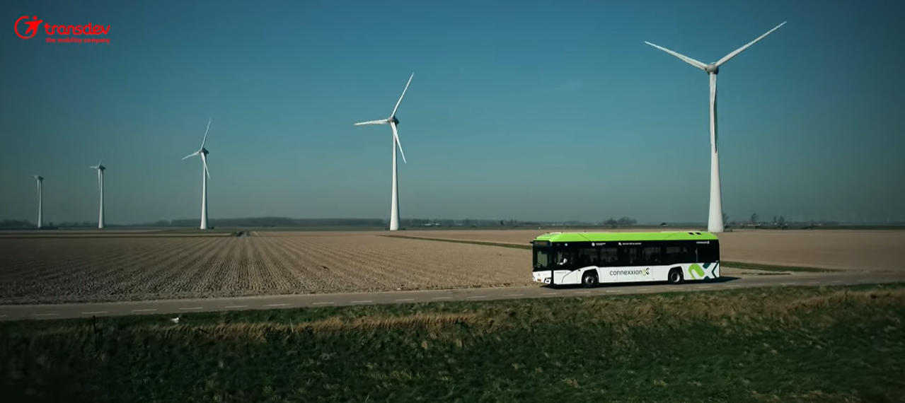 Bus conexxion qui reoule devant un champ d'éoliennes