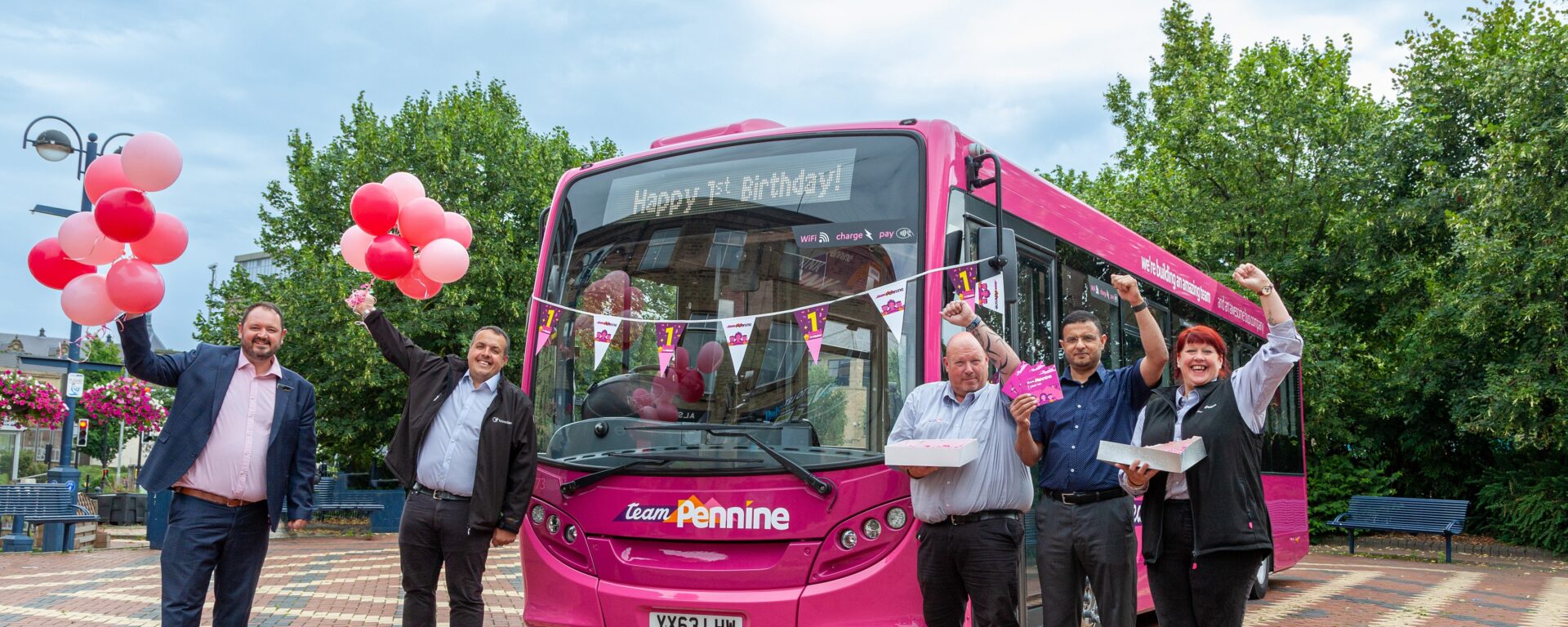 Team Pennine members holding pink baloons, standing in front of a pink bus