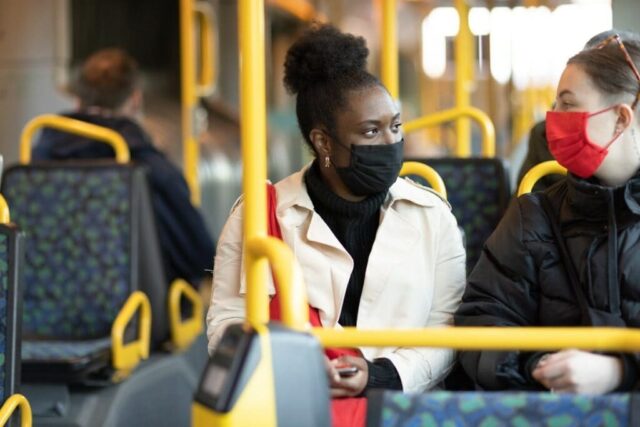 Two young women sitting talking with red and black masks in a bus