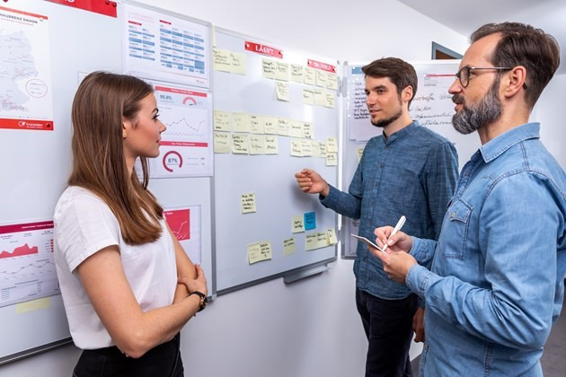 trois personnes en réflexion devant un tableau blanc