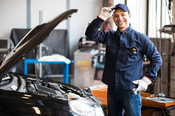 Mécanicien qui porte une casquette debout dans un garage devant un capot ouvert