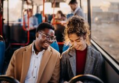 jeune homme noir avec des lunette et jeune femme blanche avec un chignon souriants assis passagers d'un bus