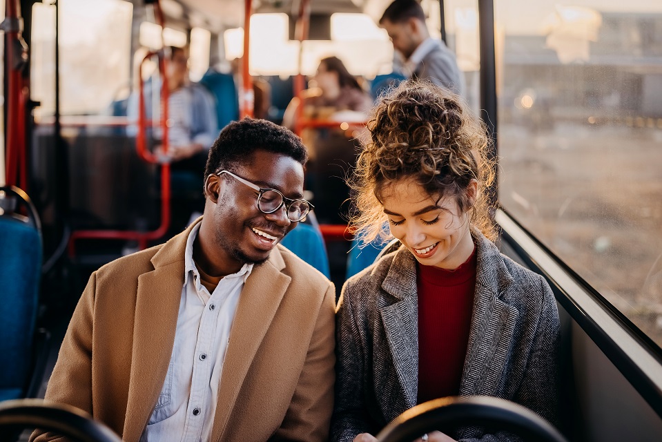 jeune homme noir avec des lunette et jeune femme blanche avec un chignon souriants assis passagers d'un bus