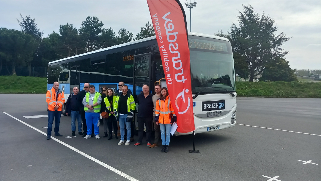 Groupe de conducteurs en gilets jaunes, debout devant un bus sur un parking